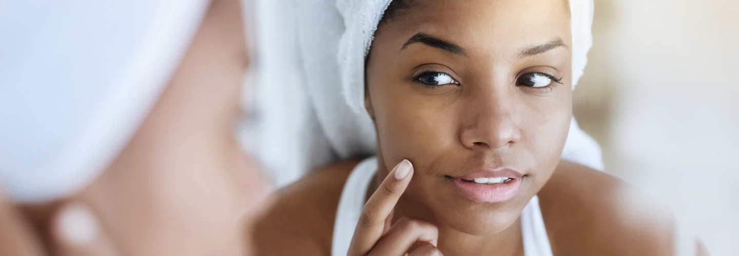 shot of a young woman inspecting her skin in front of a mirror