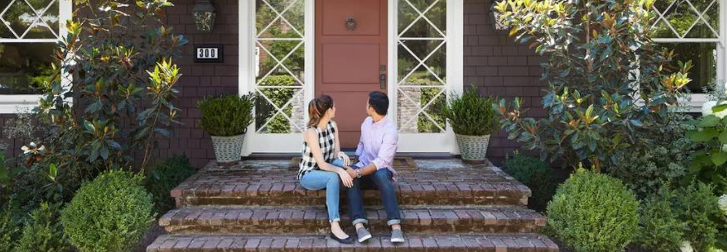 Young couple sitting on steps looking back at house.