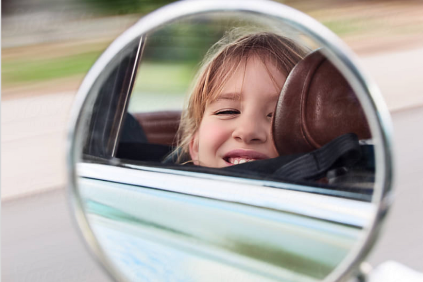 Mirror image of kid looking out car window with blurry background.