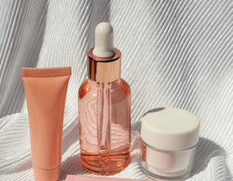 serum bottle, cosmetic tubes and container on white fabric
