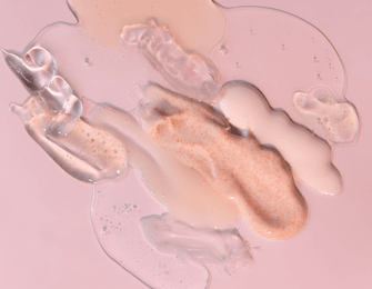 assorted liquid skincare products on pink background